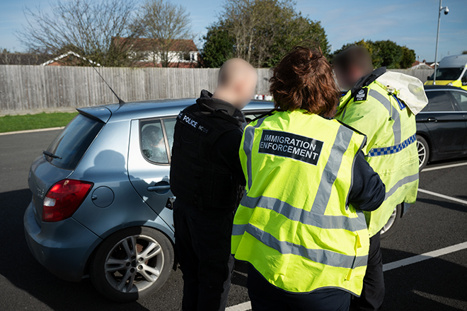 Police and Immigration officers approach a grey vehicle