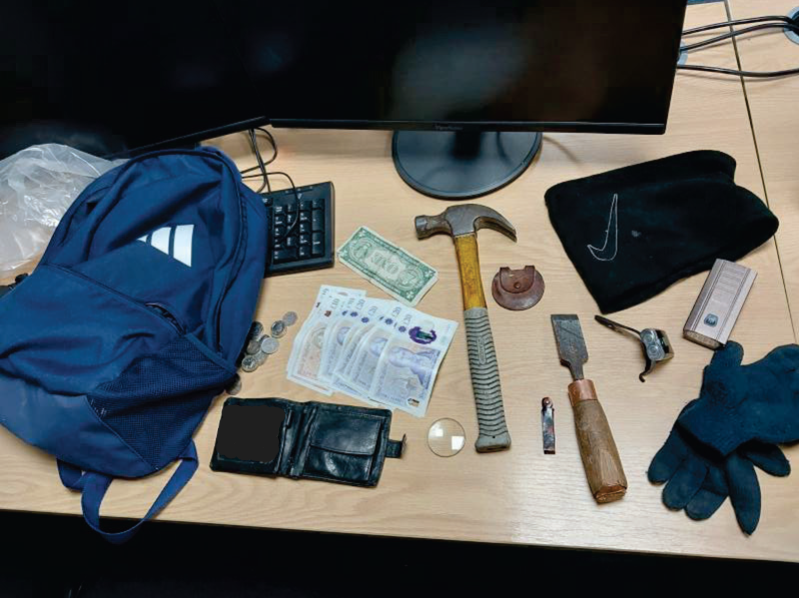 A collection of items including a blue rucksack, wallet, cash, coins, tools, and gloves laid out on a desk.