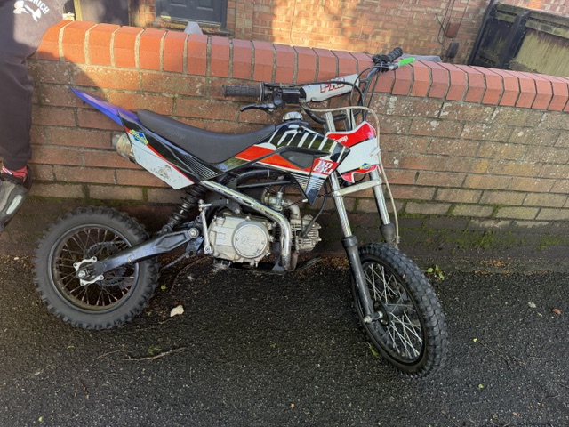 An off road red motorbike propped against a wall 