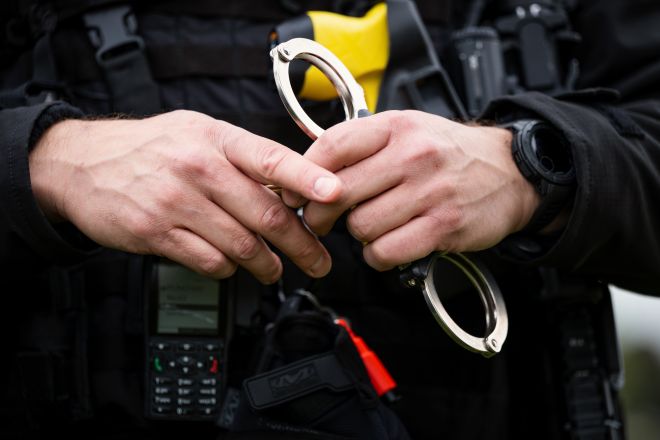 A police officer's hands holding a pair of handcuffs, with a tactical vest and radio visible.