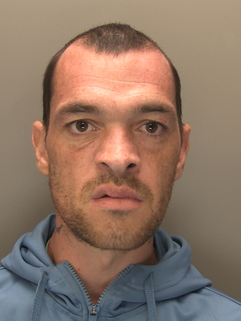 A custody image of Dean Roberts, he has dark shared hair and is wearing a blue hooded top