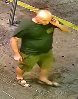 Bald man, green t-shirt with logo lefthand side of chest, khaki shorts and sandals.