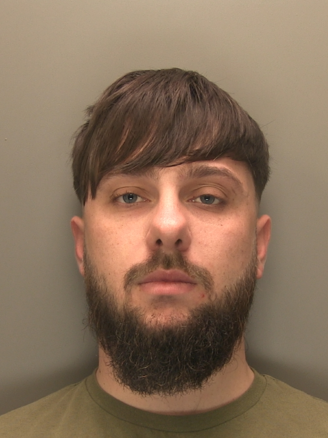 Man with long fringe, brown hair and facial hair / beard wearing an olive green t-shirt.