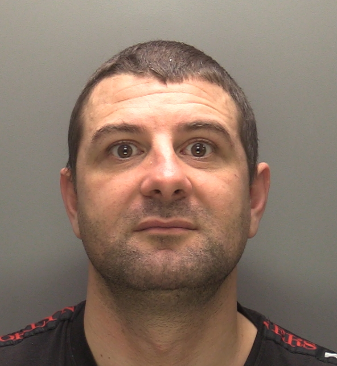 Custody image of 33-year-old Jay Savage. He is looking directly at the camera and is wearing a black t-shirt with red on the shoulders. 