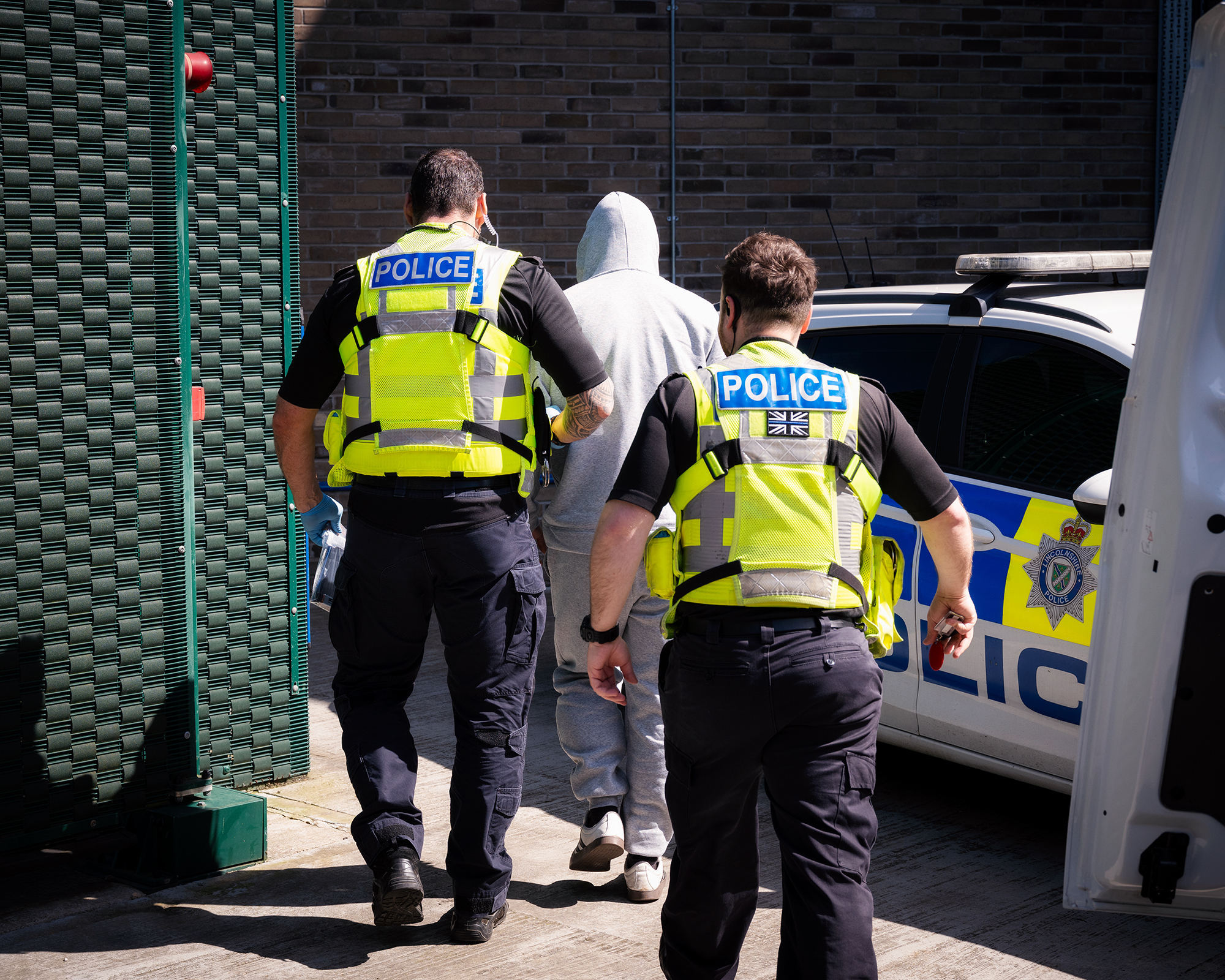 Two officers escort a suspect wearing grey joggers into custody