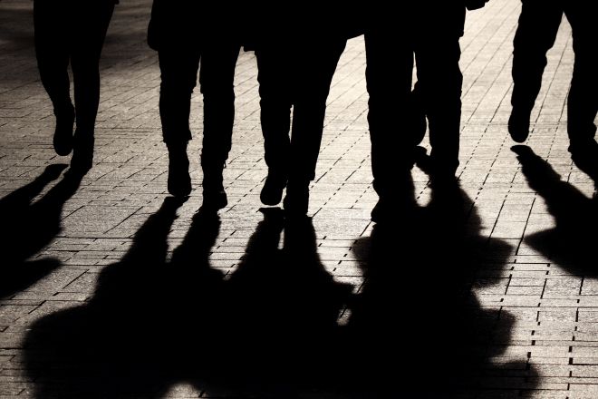 Shadowy figures of people walking down a street lit by streetlamps