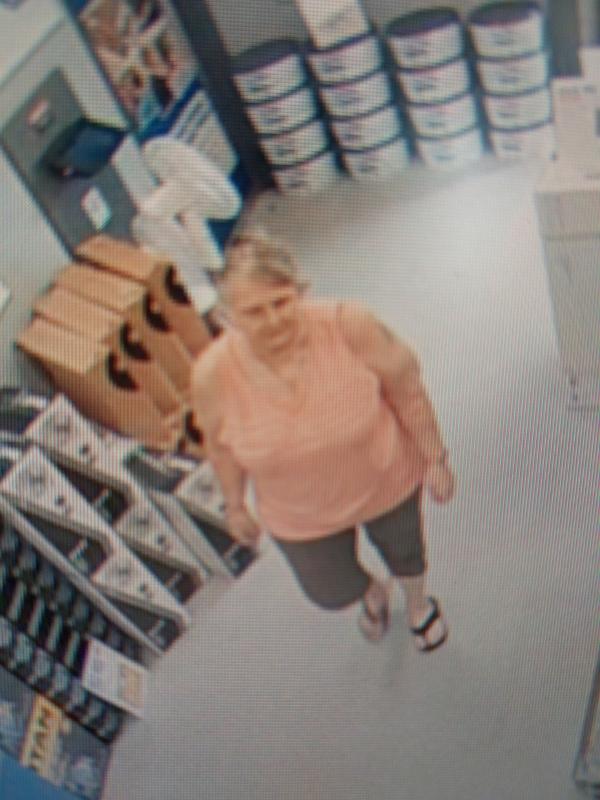 CCTV image of woman in orange top and dark coloured shorts wearing sandals. 