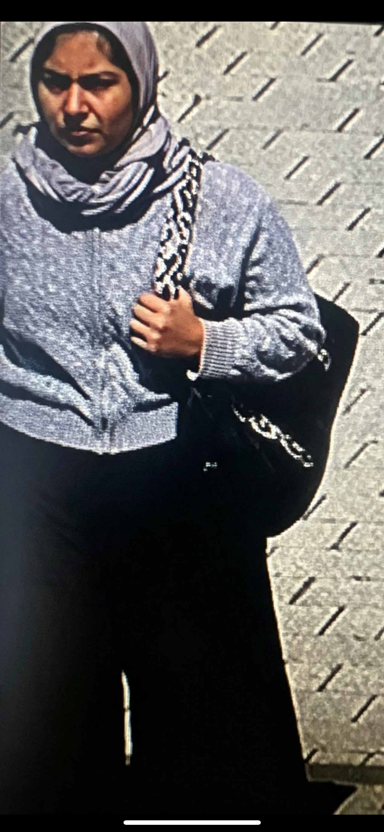 CCTV image of woman wearing a grey jacket and a hijab walking.