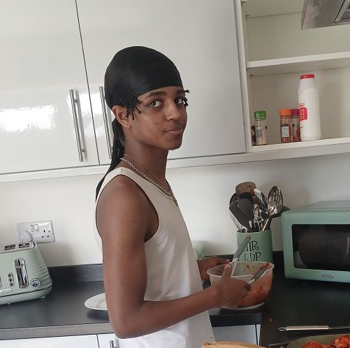 A young man in a black durag and white vest top preparing food in a modern kitchen.