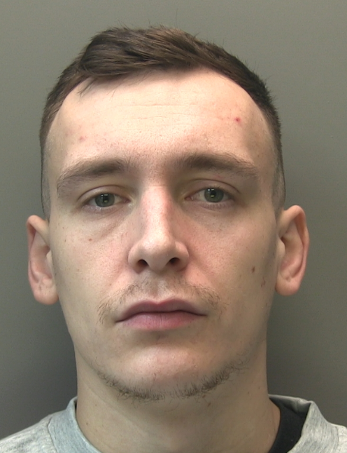 A custody image of a young white man with short brown hair, a moustache, and a neutral expression.