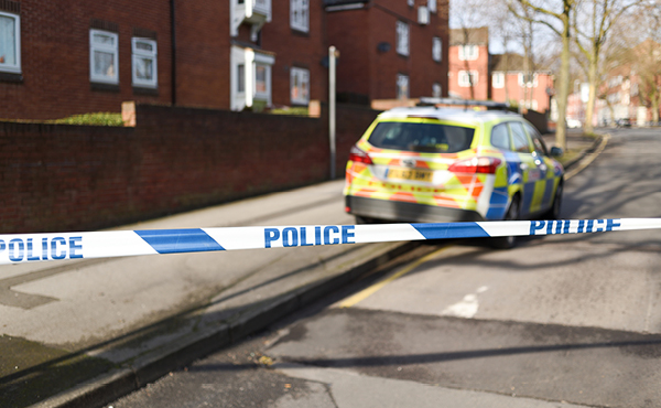 Marked police car parked outside a house. Blue and white police tape can be seen in the foreground.