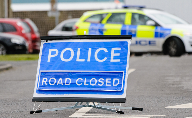 A blue police sign with the words 'Road Closed' placed on the road.