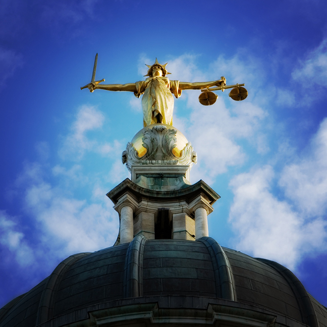 Lady Justice statue holding scales and sword against blue sky.