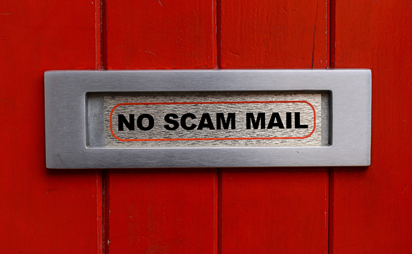 Close up of a red door with letterbox with the words 'NO SCAM MAIL'