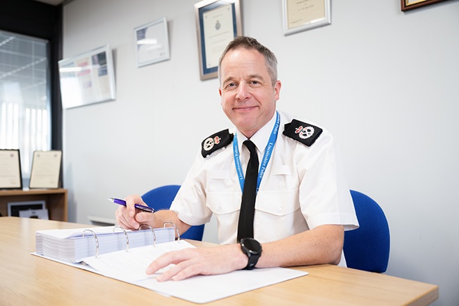 Chief Constable Paul Gibson, sitting at a desk, smiling and looking into the camera